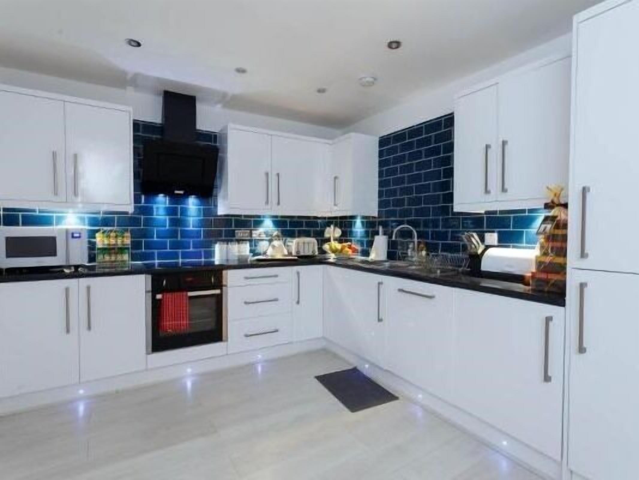 A modern kitchen with white cabinets, a black countertop, and blue-tiled backsplash.