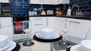 Een moderne keuken met witte kasten, een zwart aanrecht en een glazen eettafel, gedekt met witte borden en wijnglazen.