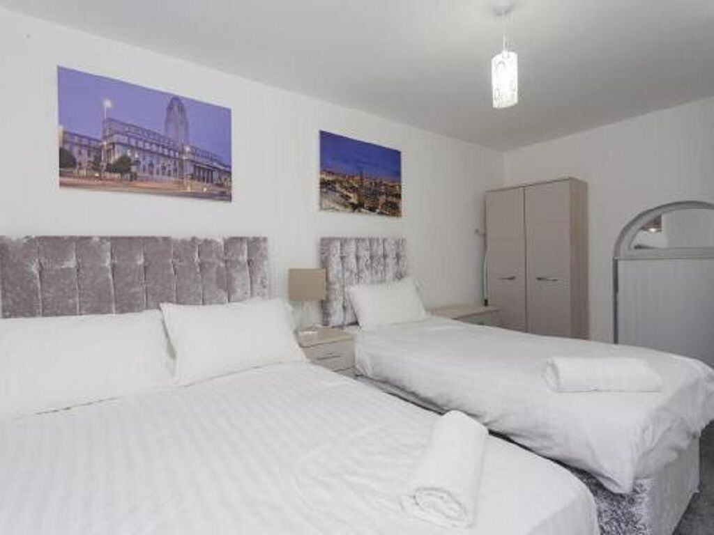A hotel room with two beds, a wardrobe, and two framed pictures on the wall.