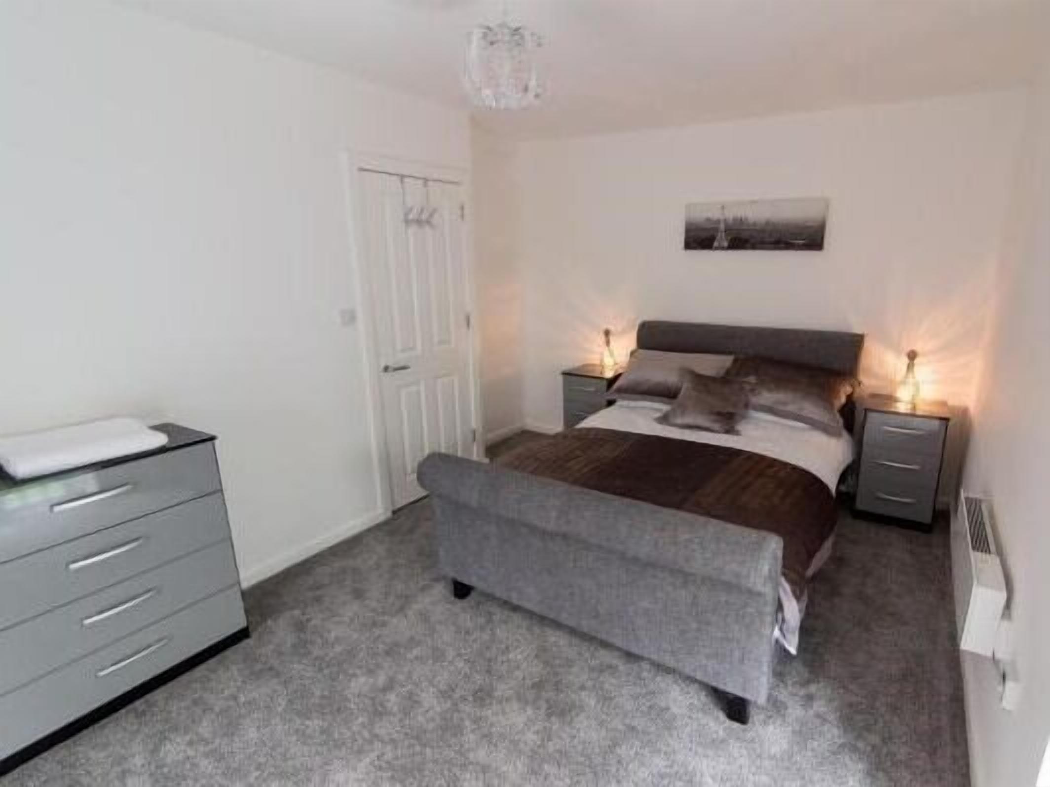 A bedroom with a bed, bedside tables, a dresser, and a door.