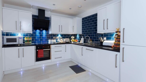 Een moderne keuken met witte kasten, een zwart aanrecht en een blauwe tegelachterwand.