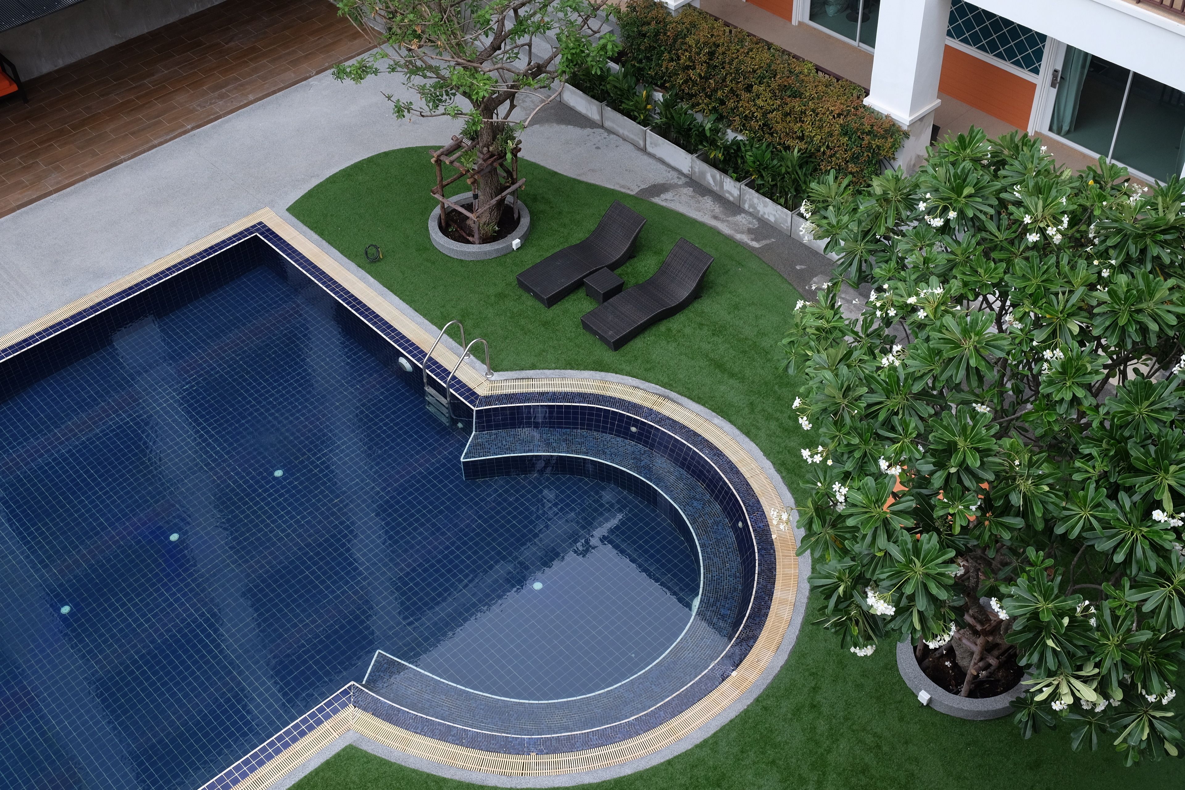 Ein Pool mit geschwungener Kante, umgeben von künstlichem Rasen und zwei Liegestühlen.