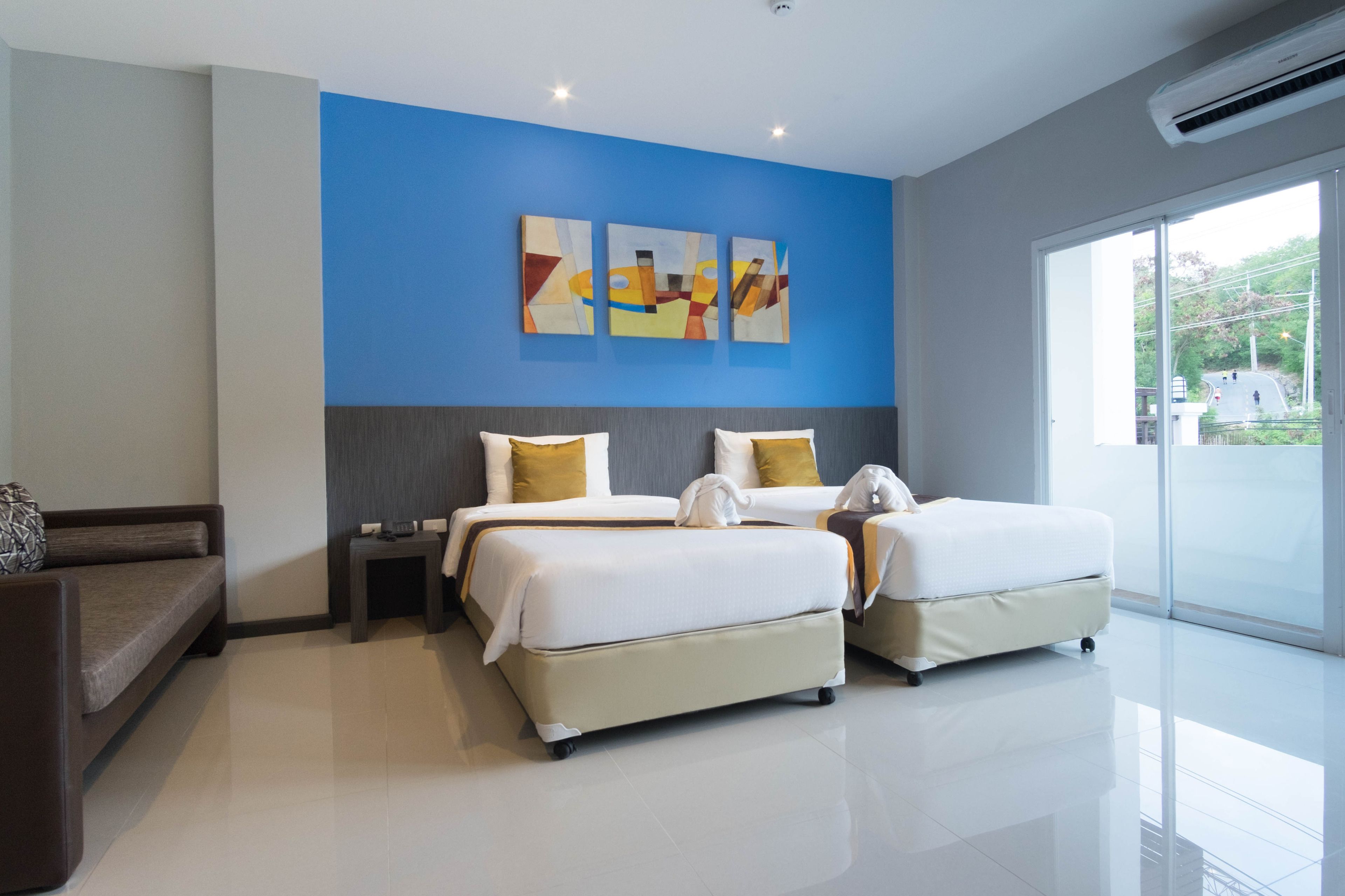 A modern hotel room with two beds, a sofa, and a large window.