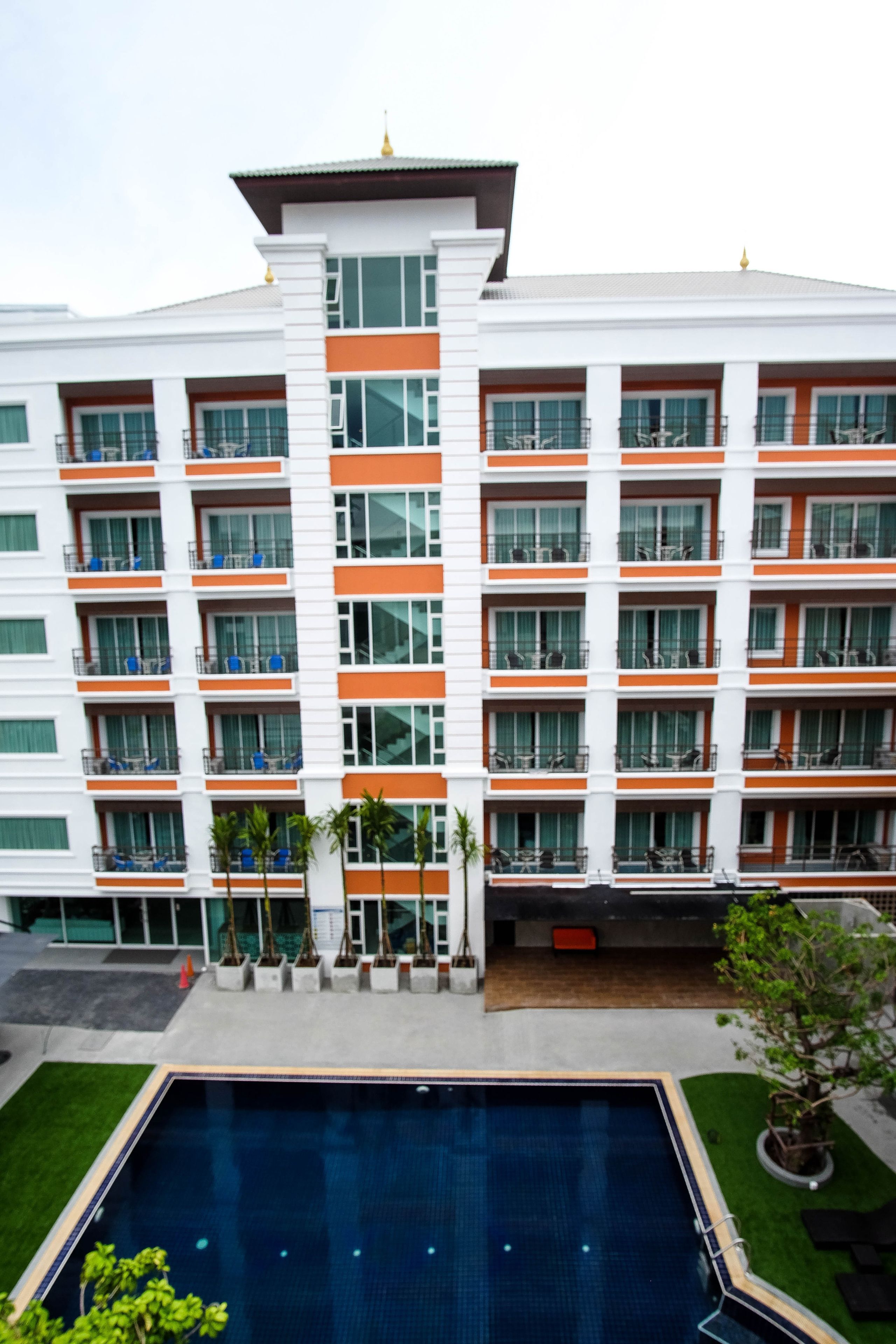 A multi-story hotel with balconies, a swimming pool, and a well-maintained lawn.