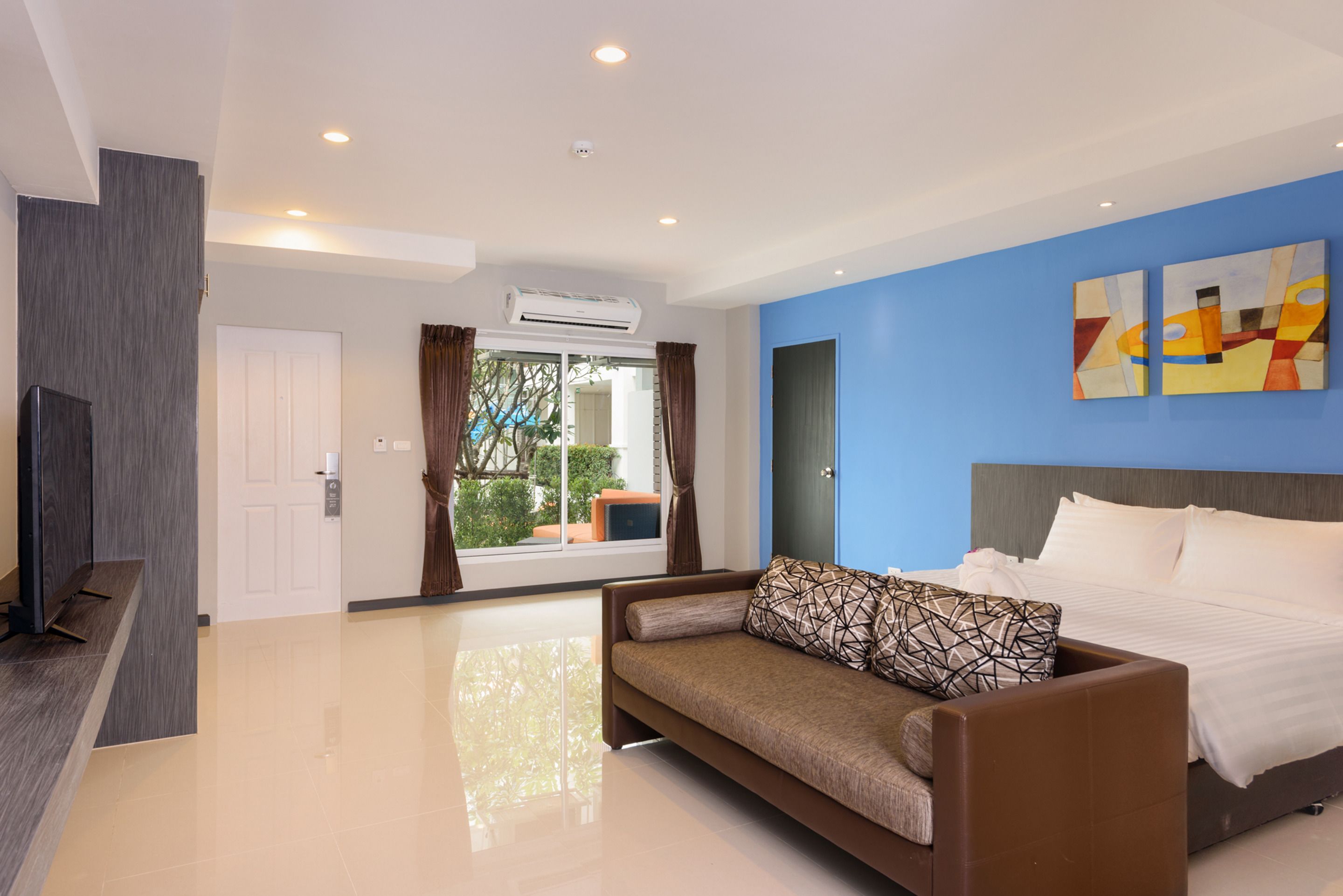 A modern hotel room with a large bed, a sofa, and a view of the outdoors.