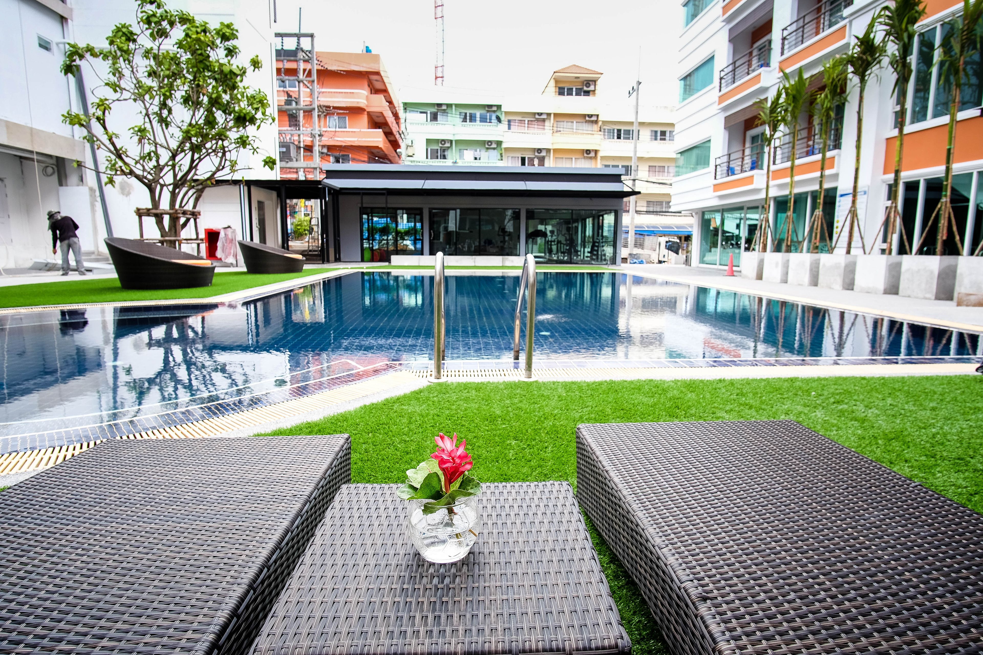 A swimming pool with a glass barrier, surrounded by artificial grass and wicker lounge chairs.