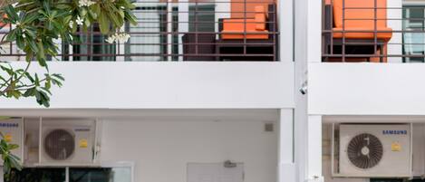 A pool area with lounge chairs and an umbrella, surrounded by a building with air conditioning units and a door.