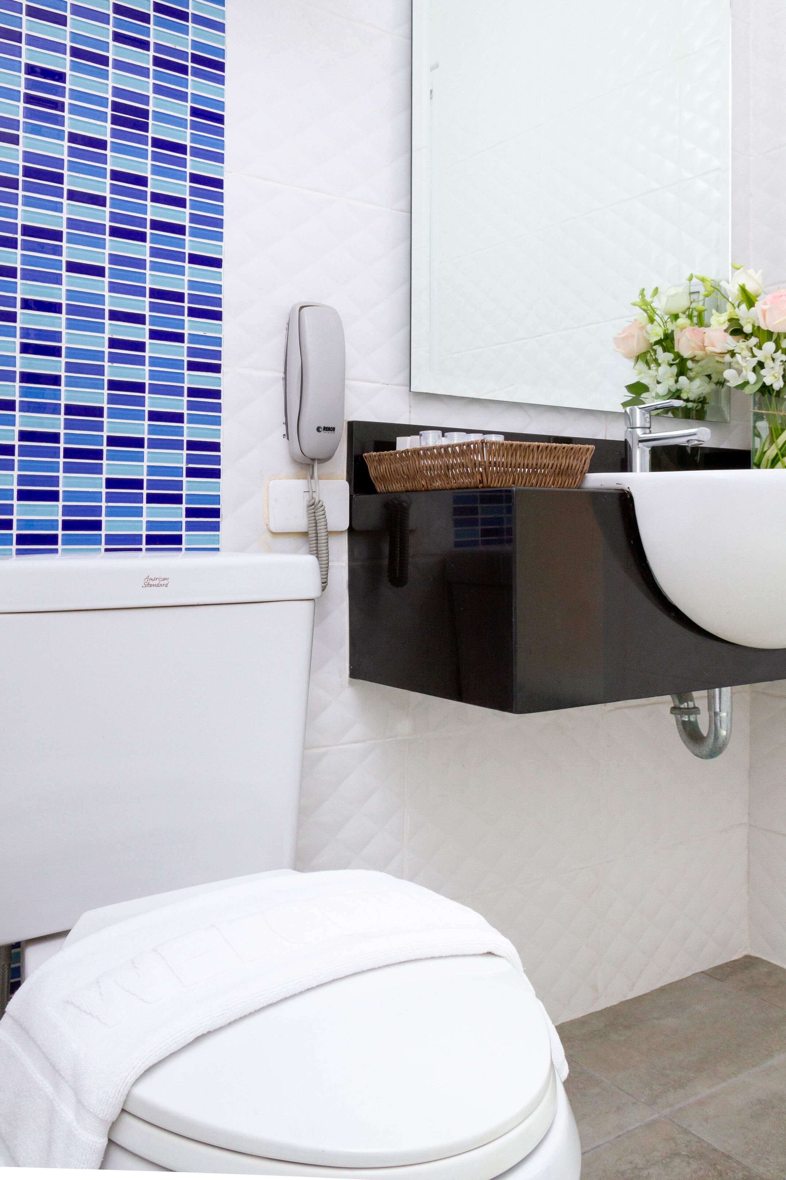 A modern bathroom with a white toilet, a white sink with a black countertop, a wicker basket, and a vase with flowers.