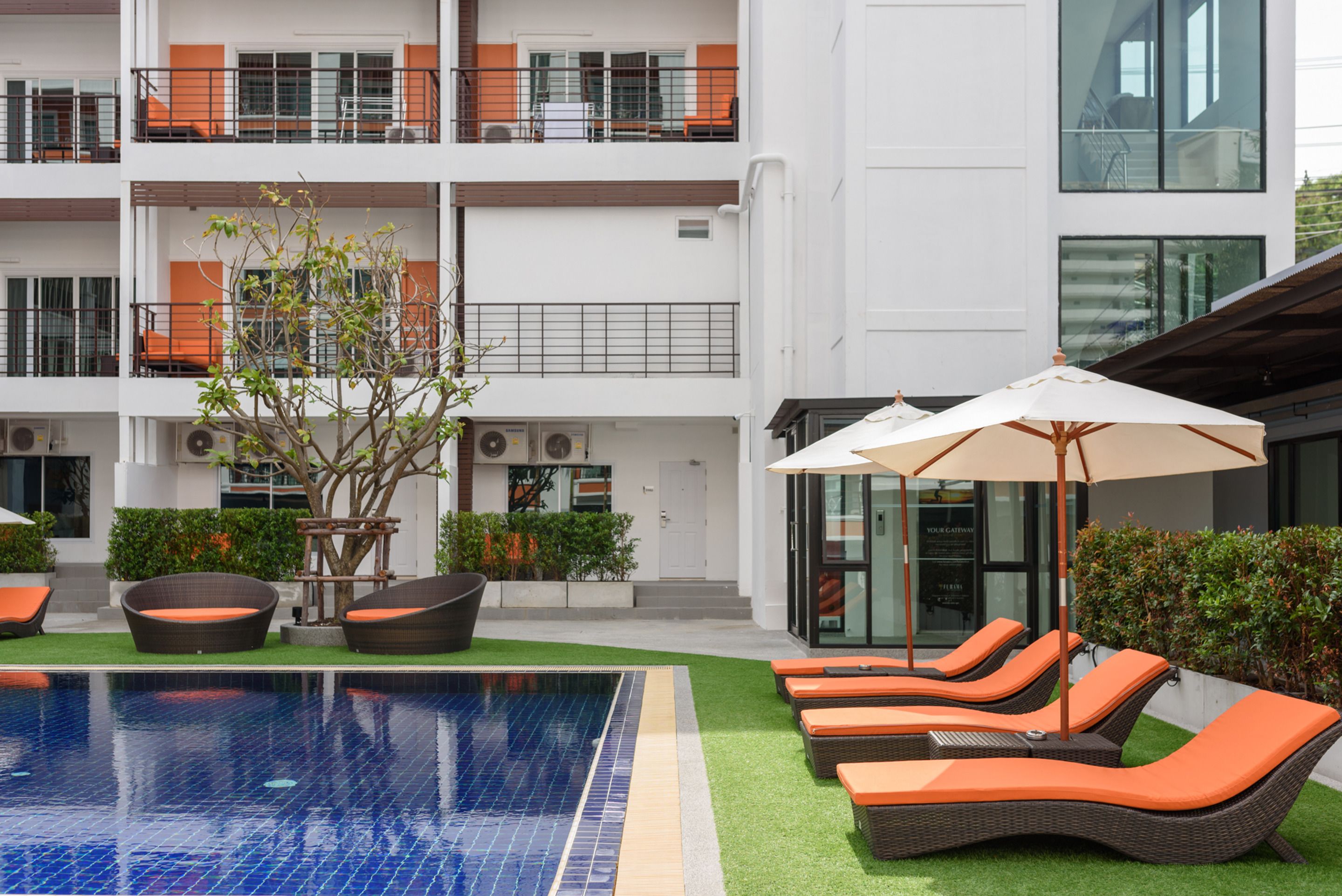 A modern hotel with a swimming pool, lounge chairs, and a well-maintained garden area.