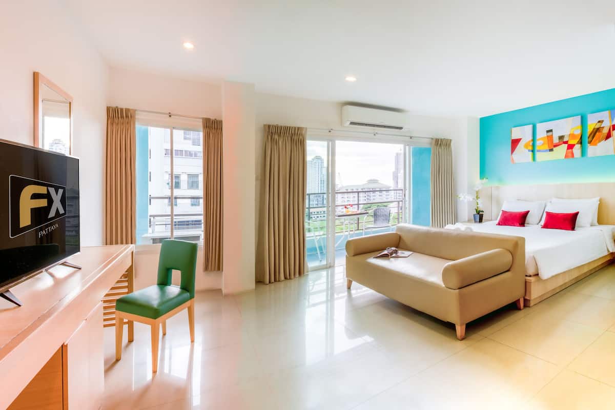 Habitación de hotel con televisión, sofá, cama, balcón con cortinas y vista a edificios.