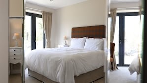 A hotel room with a large bed, two bedside tables, a nightstand, and a view of the outdoors through a door. - The 3 Millstones Inn (Clitheroe)