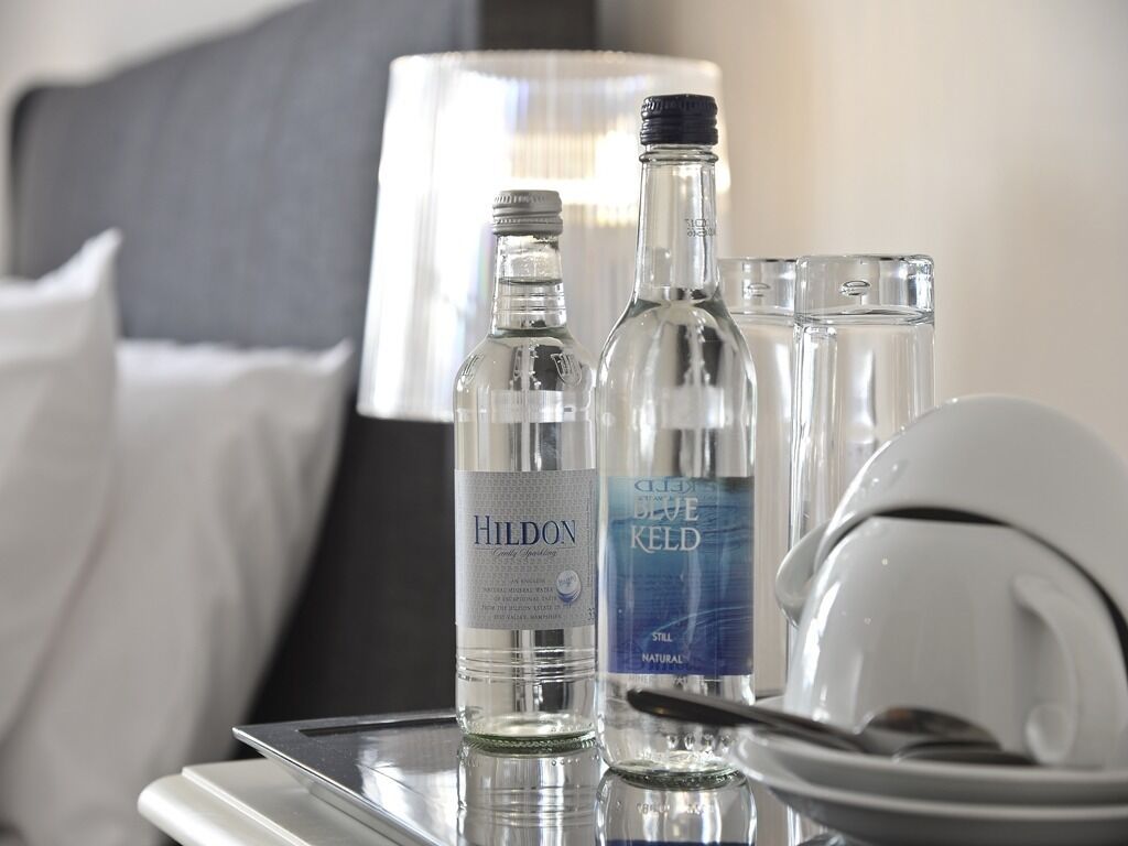 A hotel room with a bed, a bedside table with two bottles of water, a glass, and a white helmet.