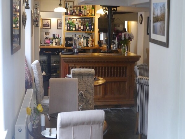 Zona de bar con mostrador de madera, taburetes y un área de estar con sofá y sillones.