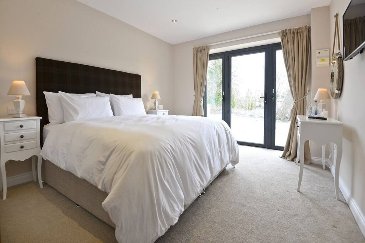 A bedroom with a large bed, two bedside tables with lamps, a TV, and a sliding glass door to the outside.