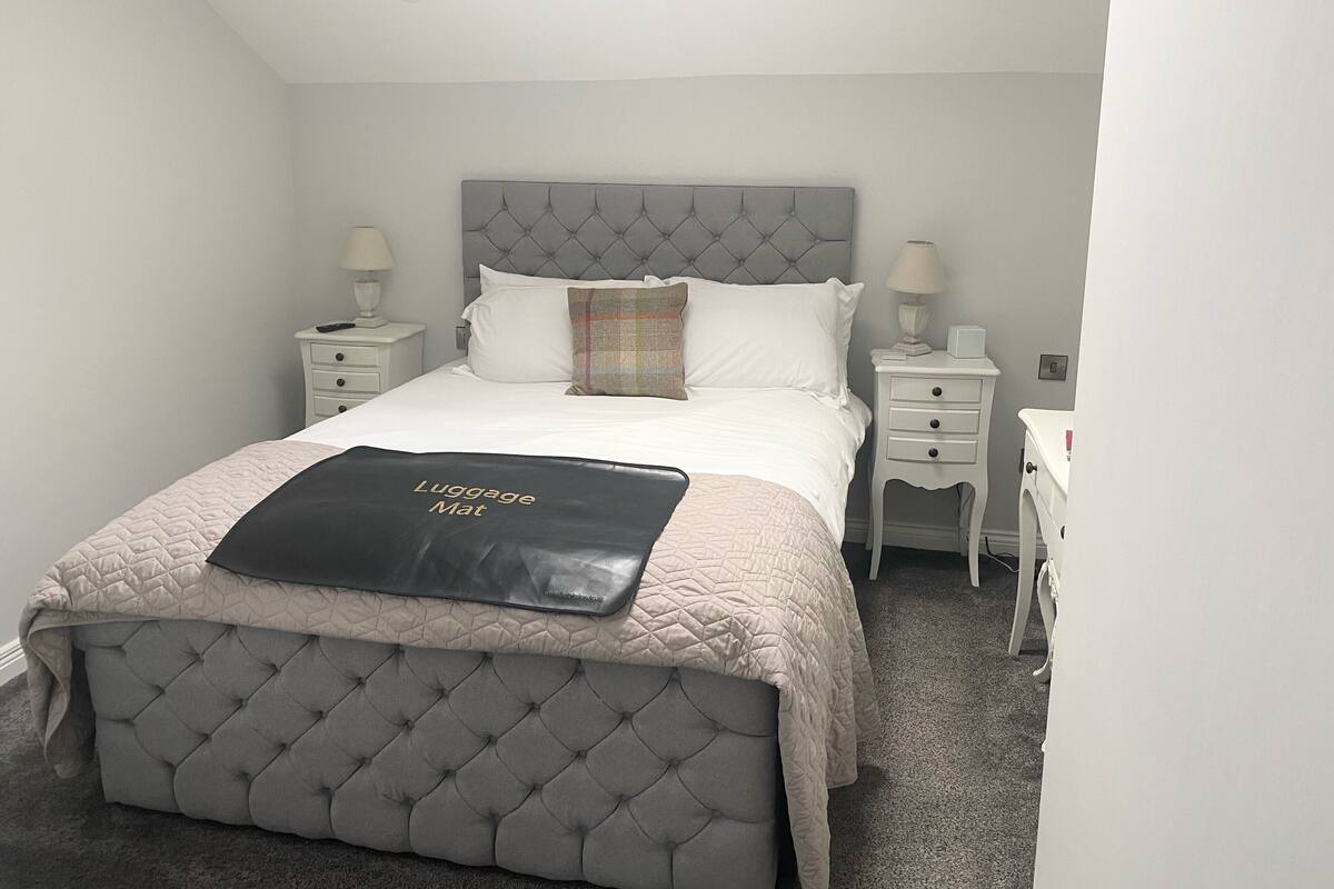 A neatly arranged bedroom with a tufted headboard, white bedding, and a luggage mat on the bed.