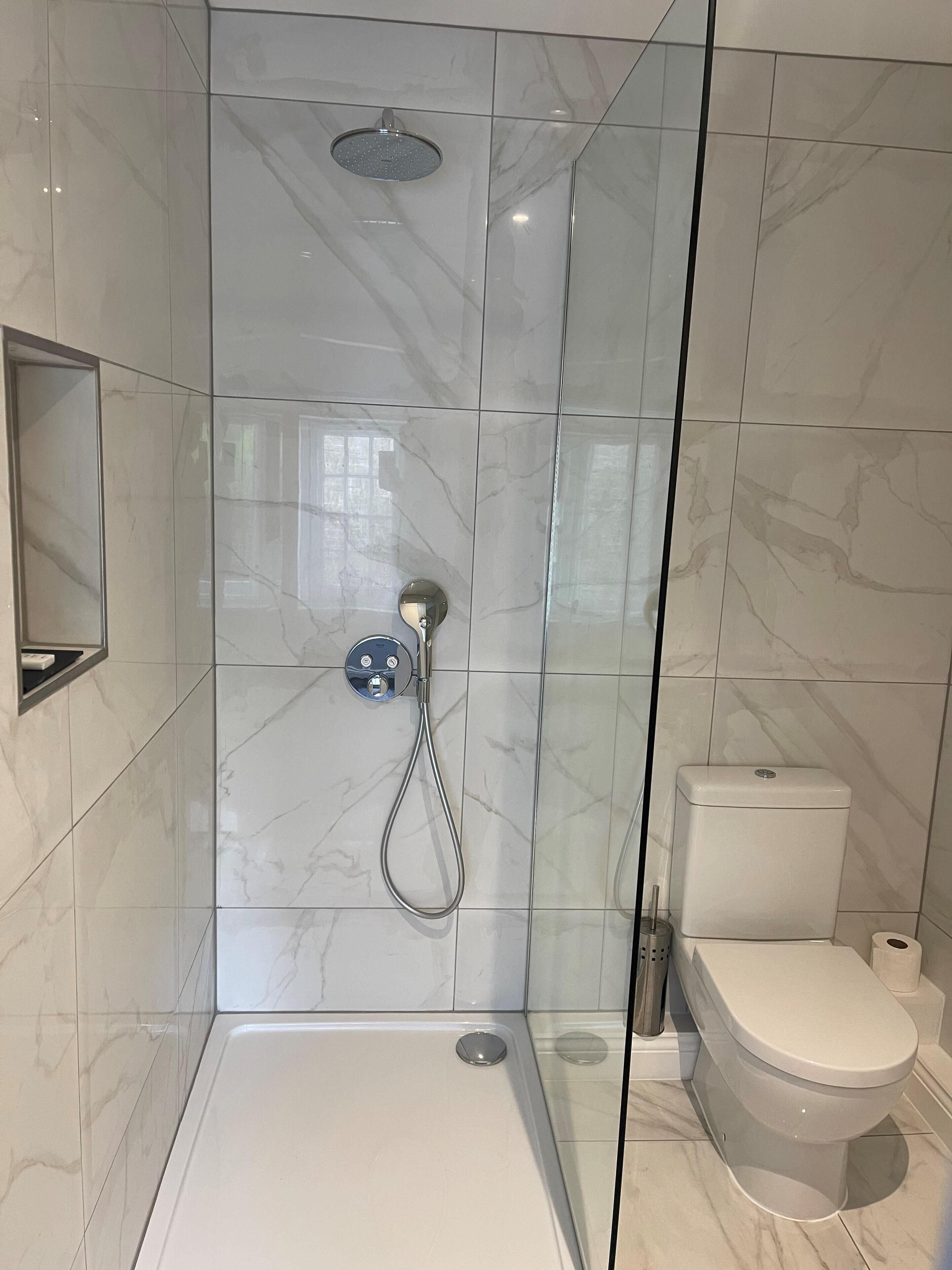 A modern bathroom with a glass-enclosed shower, a toilet, and a marble-tiled wall.