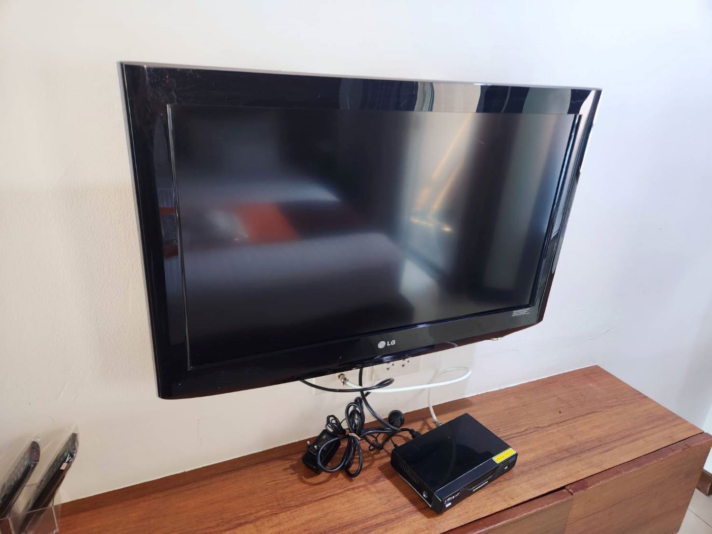 A flat-screen TV mounted on a wall, connected to a wooden entertainment unit with a black electronic device on it.