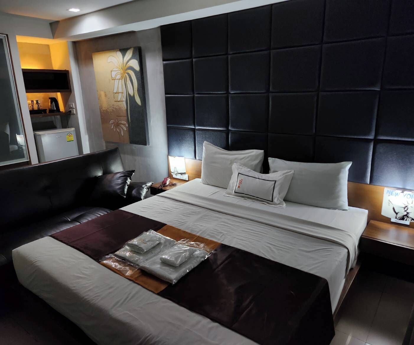 Una habitación de hotel moderna con una cama grande, un cabecero oscuro y una mesita de noche con lámpara.