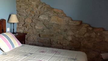 Un dormitorio con pared de piedra, cabecera de madera, mesita de noche con lámpara y almohadas a rayas.