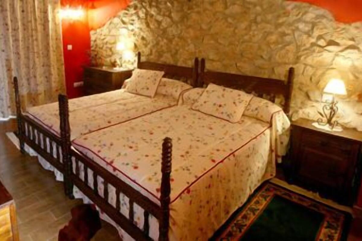 Un dormitorio con una cama doble, pared de piedra, mesita de noche con lámpara y una silla de madera.