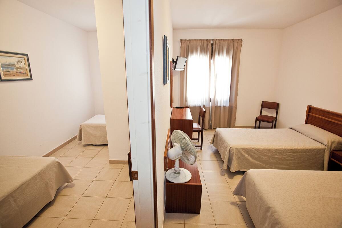 Una habitación de hotel con dos camas, un escritorio, una silla y un ventilador de pie.
