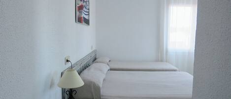 A hotel room with two beds, a nightstand with a lamp, a painting on the wall, and a window with curtains.