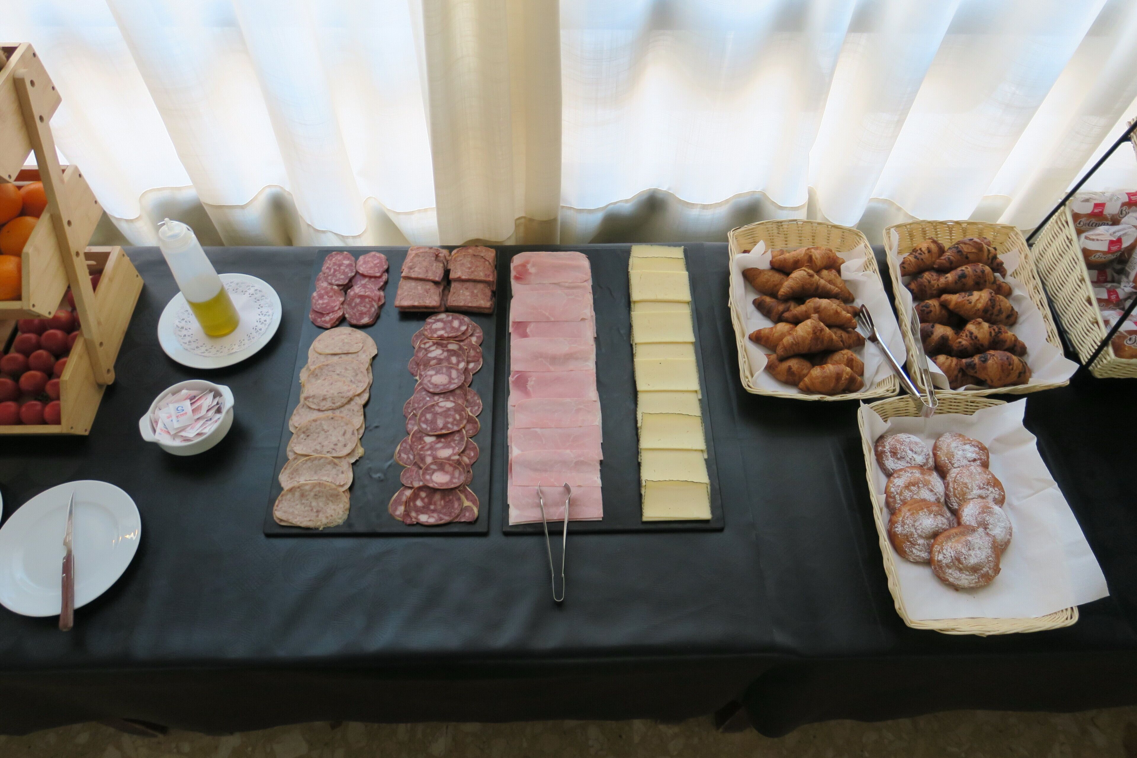 Una mesa de buffet con diversos alimentos, incluyendo fiambres, quesos y pastelería.