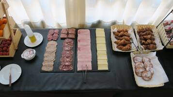 Una mesa de buffet con diversos alimentos, incluyendo fiambres, quesos y pastelería.
