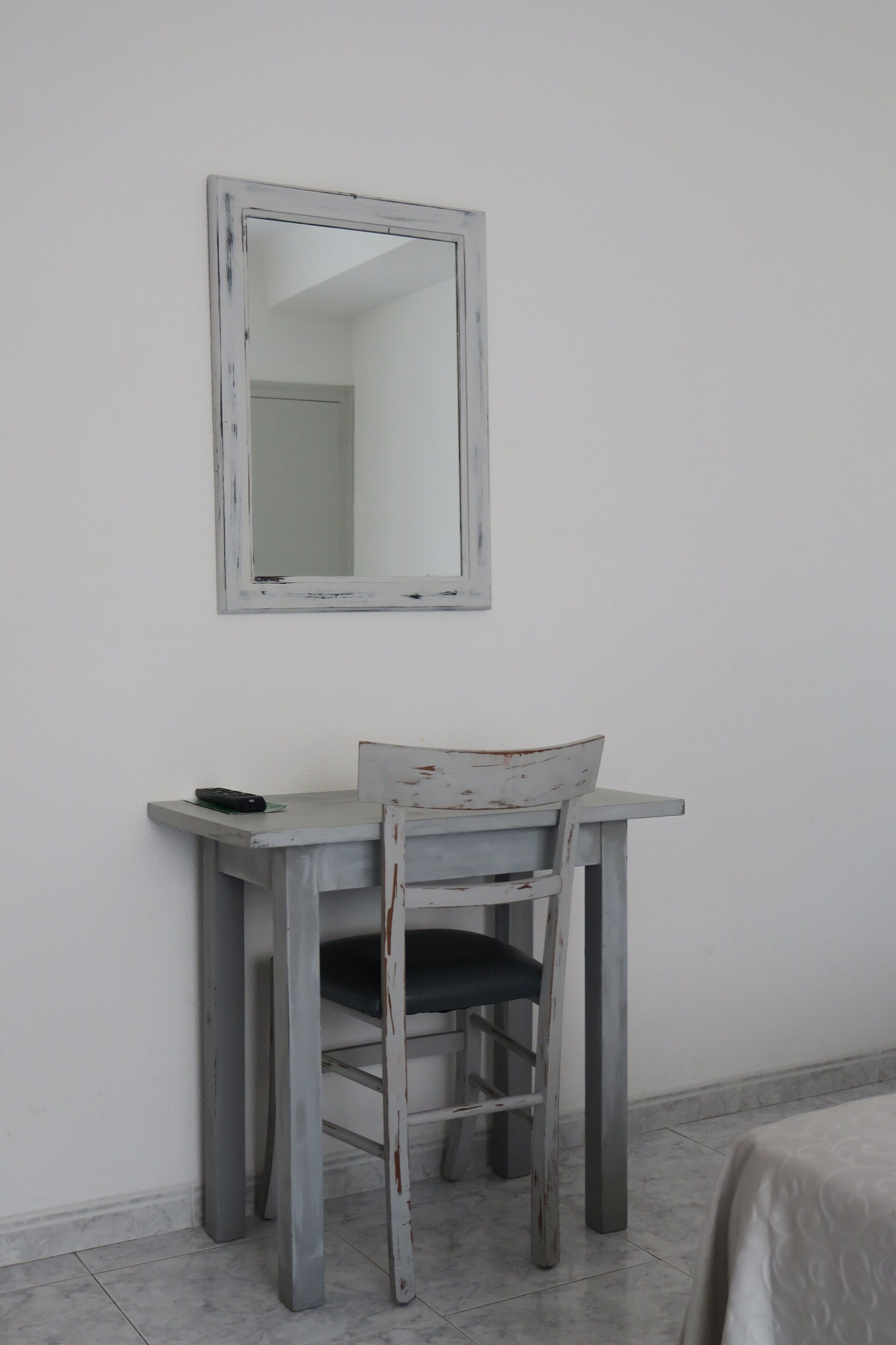 A small, white-painted desk with a chair and a mirror above it.