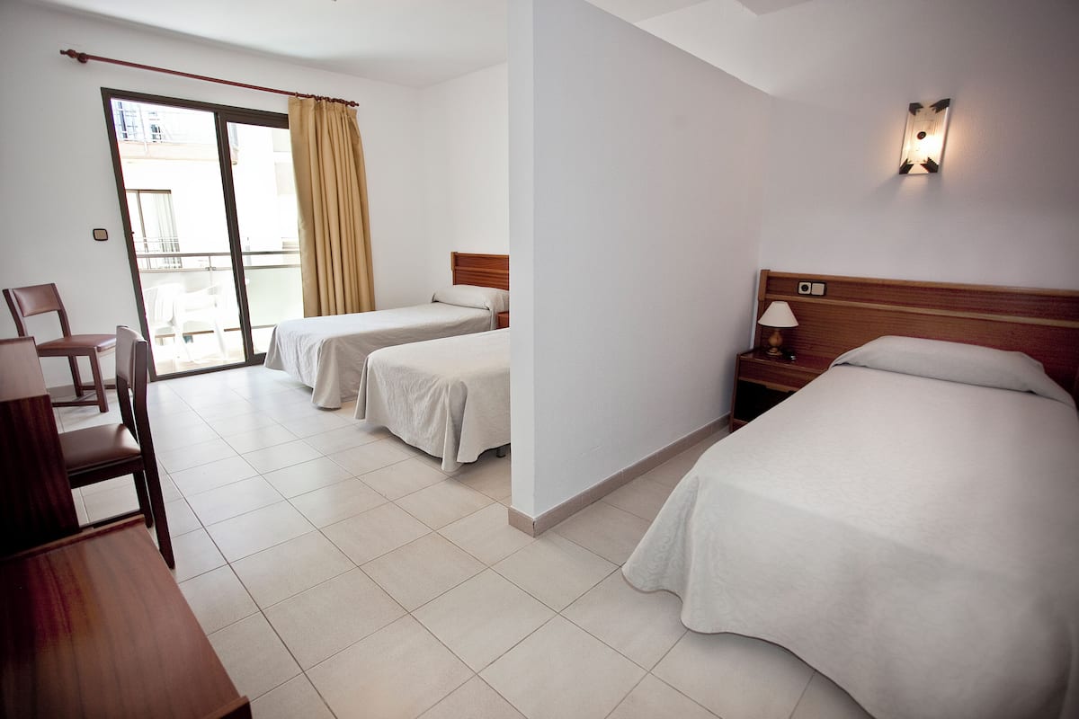 Habitación de hotel con dos camas, un escritorio, una silla y puerta corrediza a un balcón.