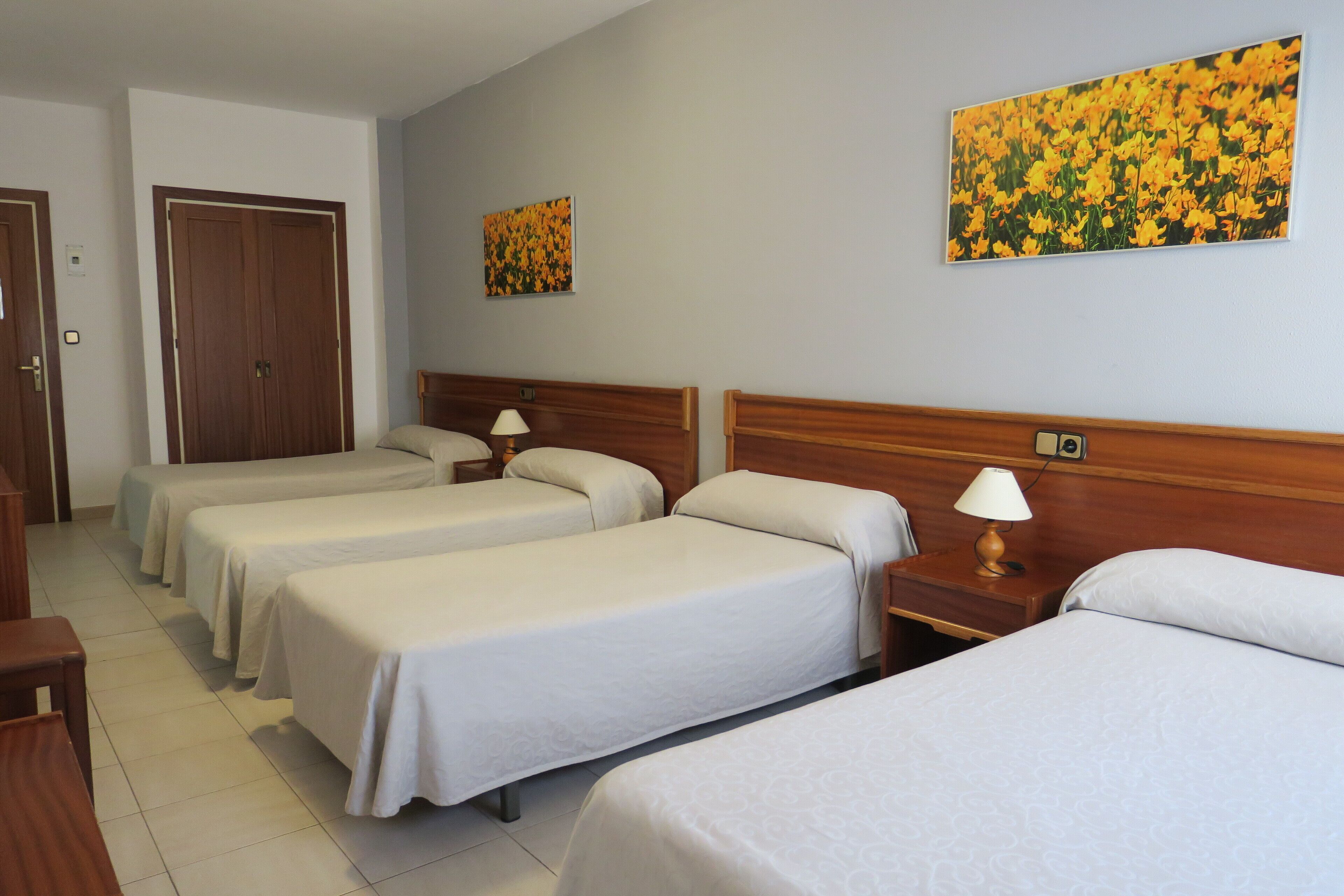 A hotel room with four single beds, wooden headboards, and bedside tables with lamps.