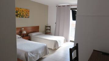 Habitación de hotel con dos camas, cabecera de madera, mesita de noche con lámpara, una silla y un cuadro en la pared.