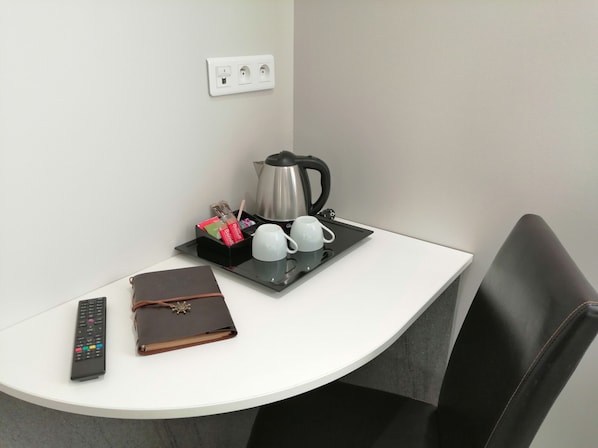 A small, clean room with a white table, a black tray with a coffee pot, cups, and a remote control.