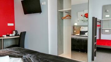 Een hotelkamer met een bed, een bureau met een stoel, een aan de muur bevestigde televisie en een spiegel die de kamer weerspiegelt.