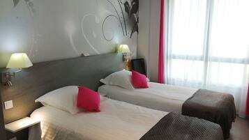 Habitación de hotel con dos camas, cabeceros, mesitas de noche con lámparas, una silla y un ventanal con cortinas.