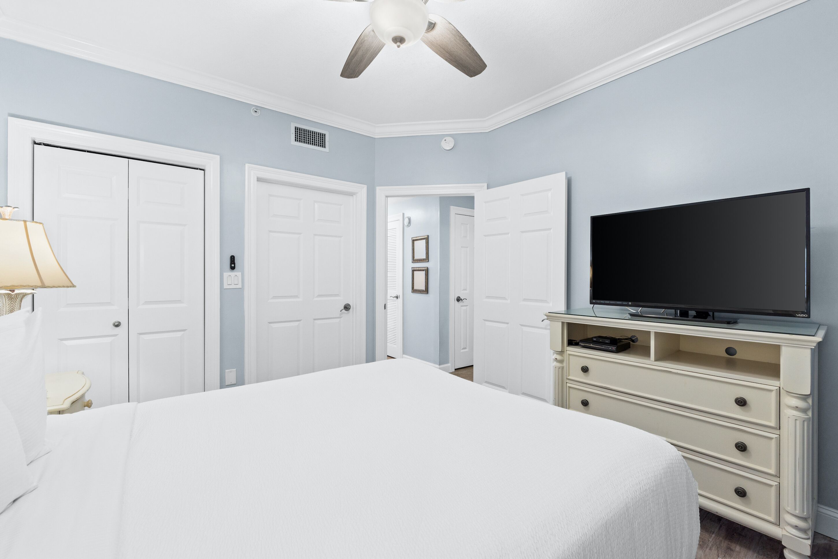 A bedroom with a bed, a TV on a dresser, and two doors.