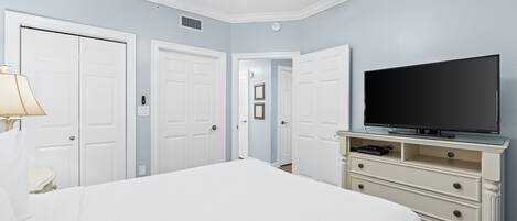 A bedroom with a bed, a TV on a dresser, and two doors.