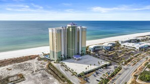 A high-rise hotel with multiple floors, a parking lot, and a beach view.