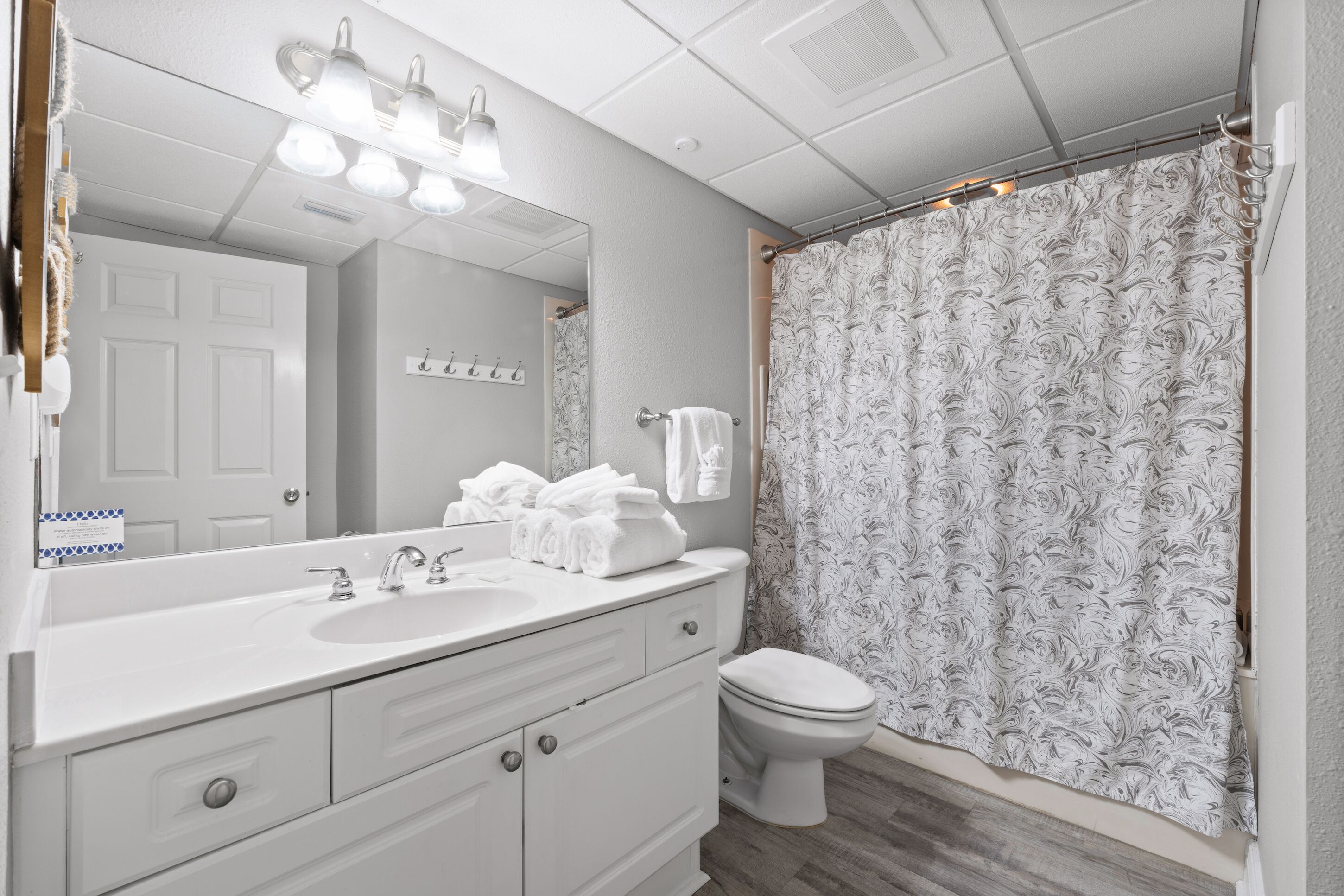 A bathroom with a white sink, mirror, and toilet, and a shower curtain with a swirl pattern.