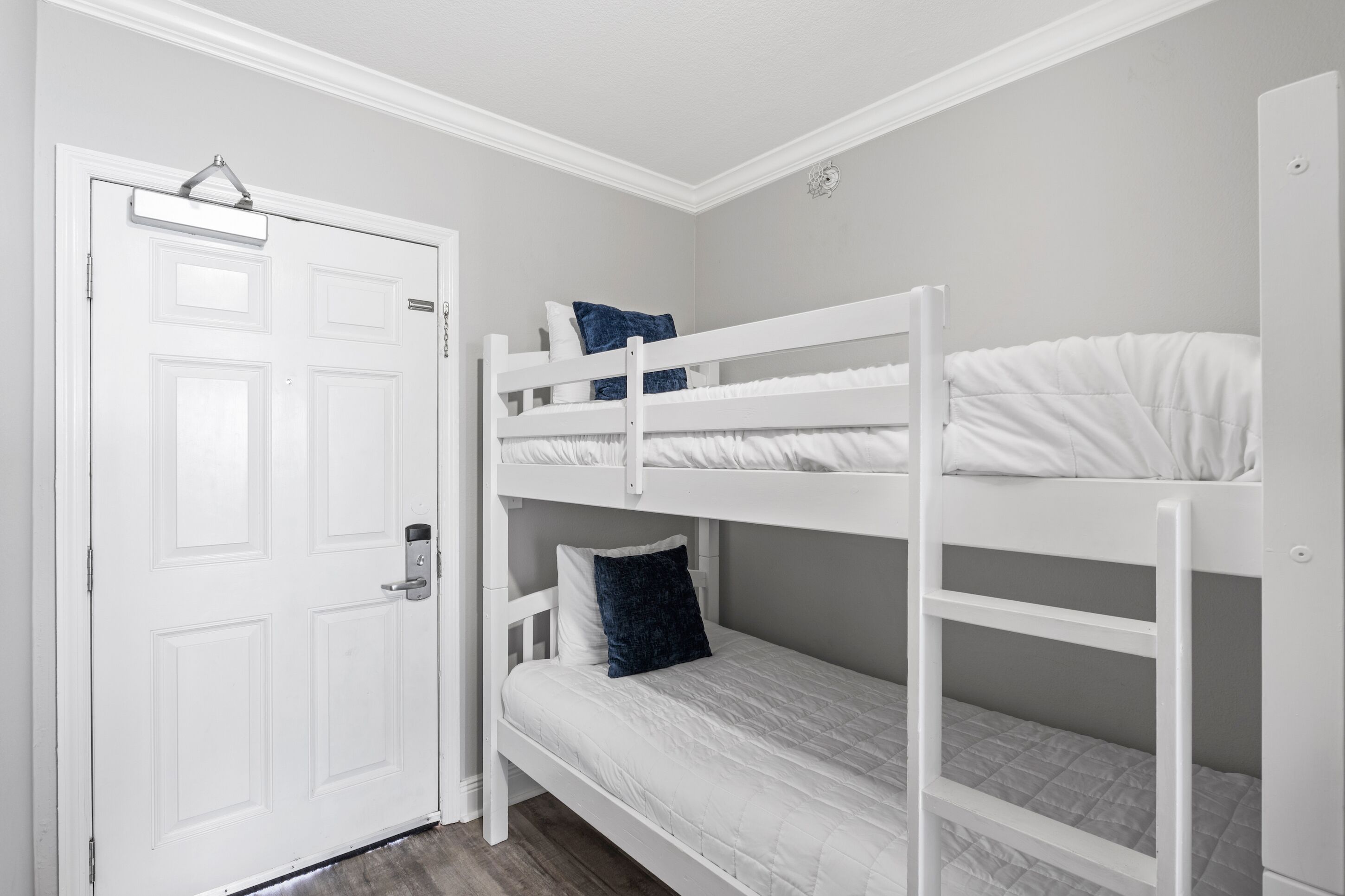 Ein Schlafsaalzimmer mit Etagenbetten, einer weißen Tür und einem kleinen Fenster.