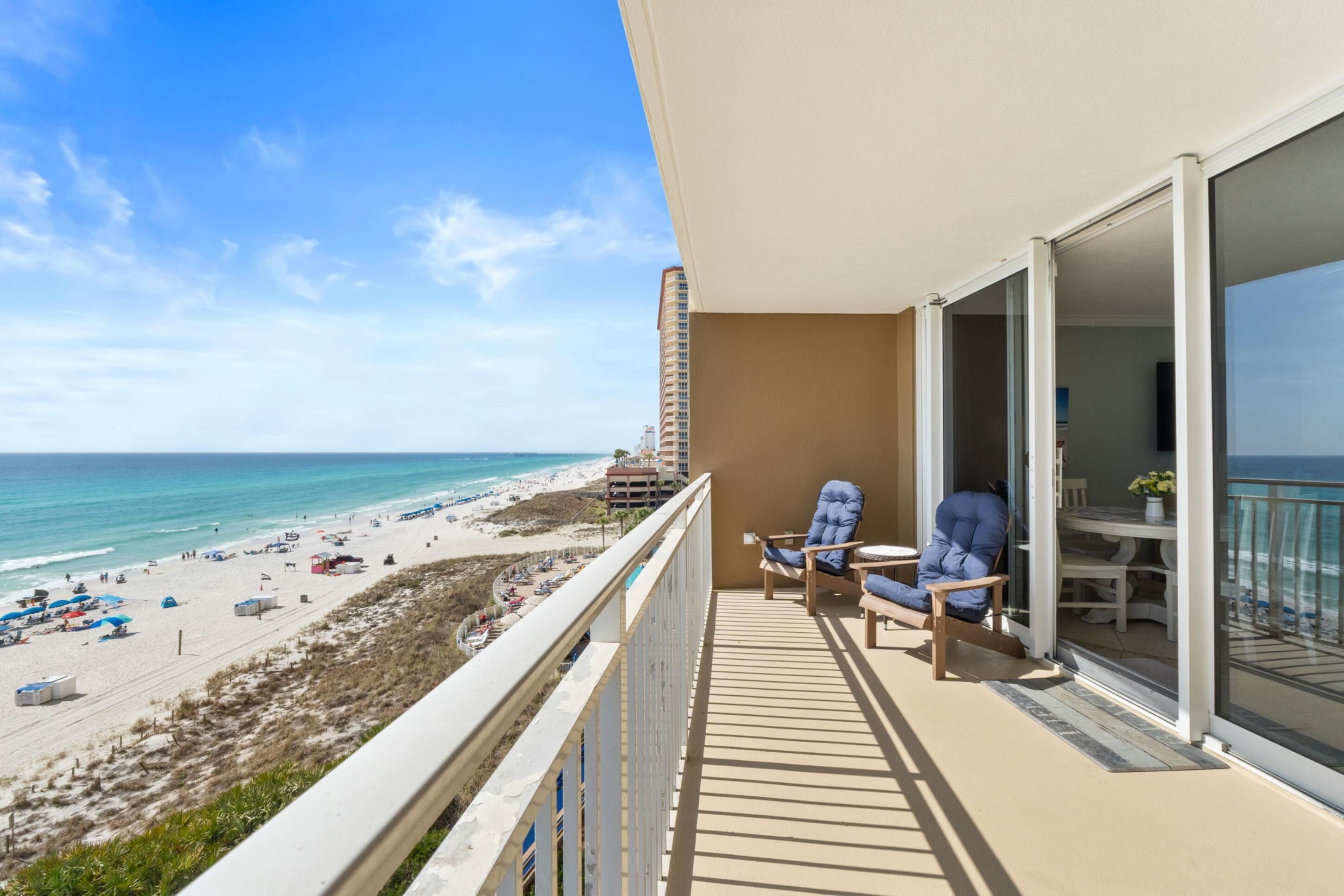 A balcony with a view of the beach and ocean, a table, and two chairs.