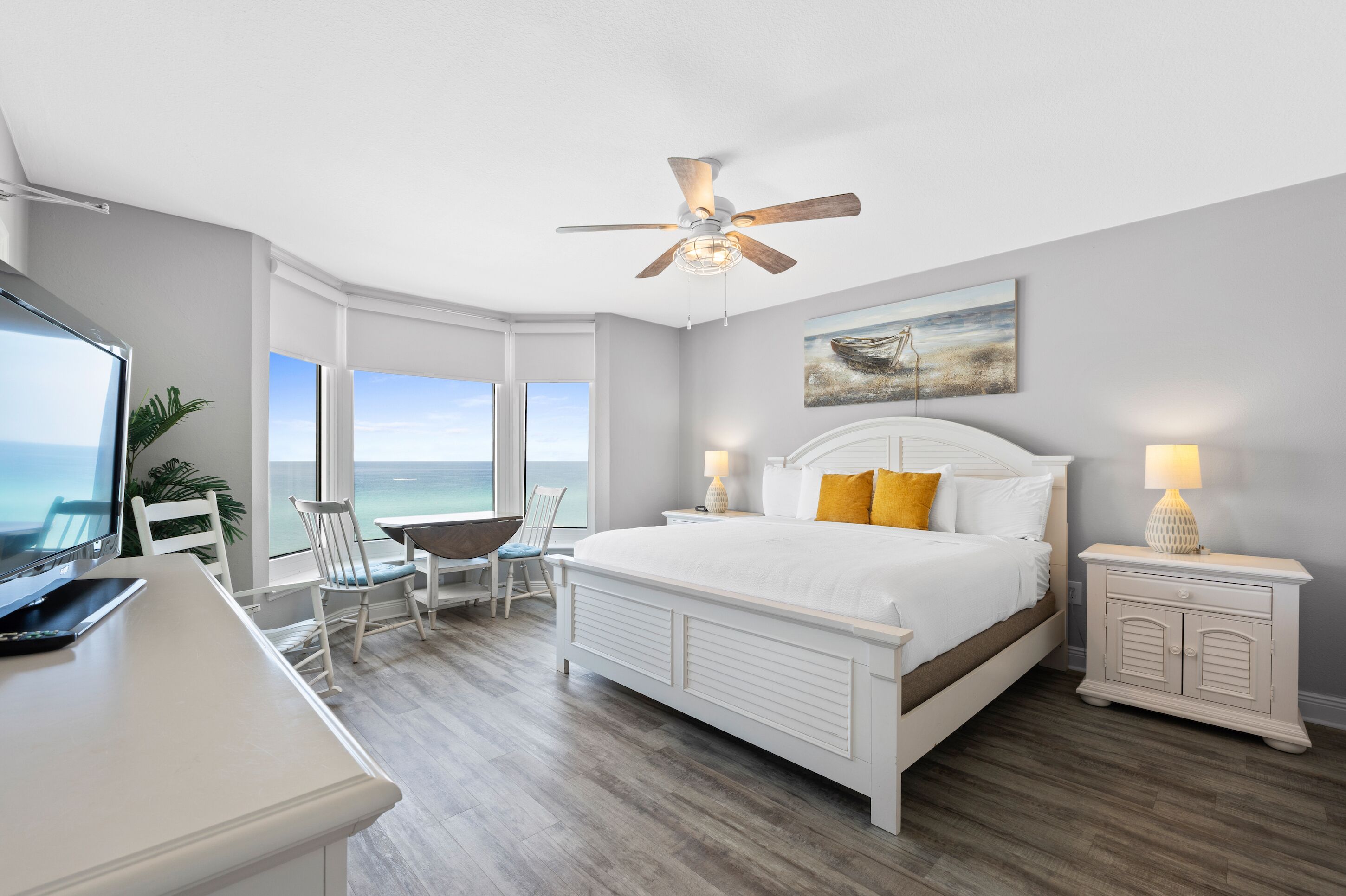 A bedroom with a large bed, a desk, a chair, a nightstand, and a ceiling fan.