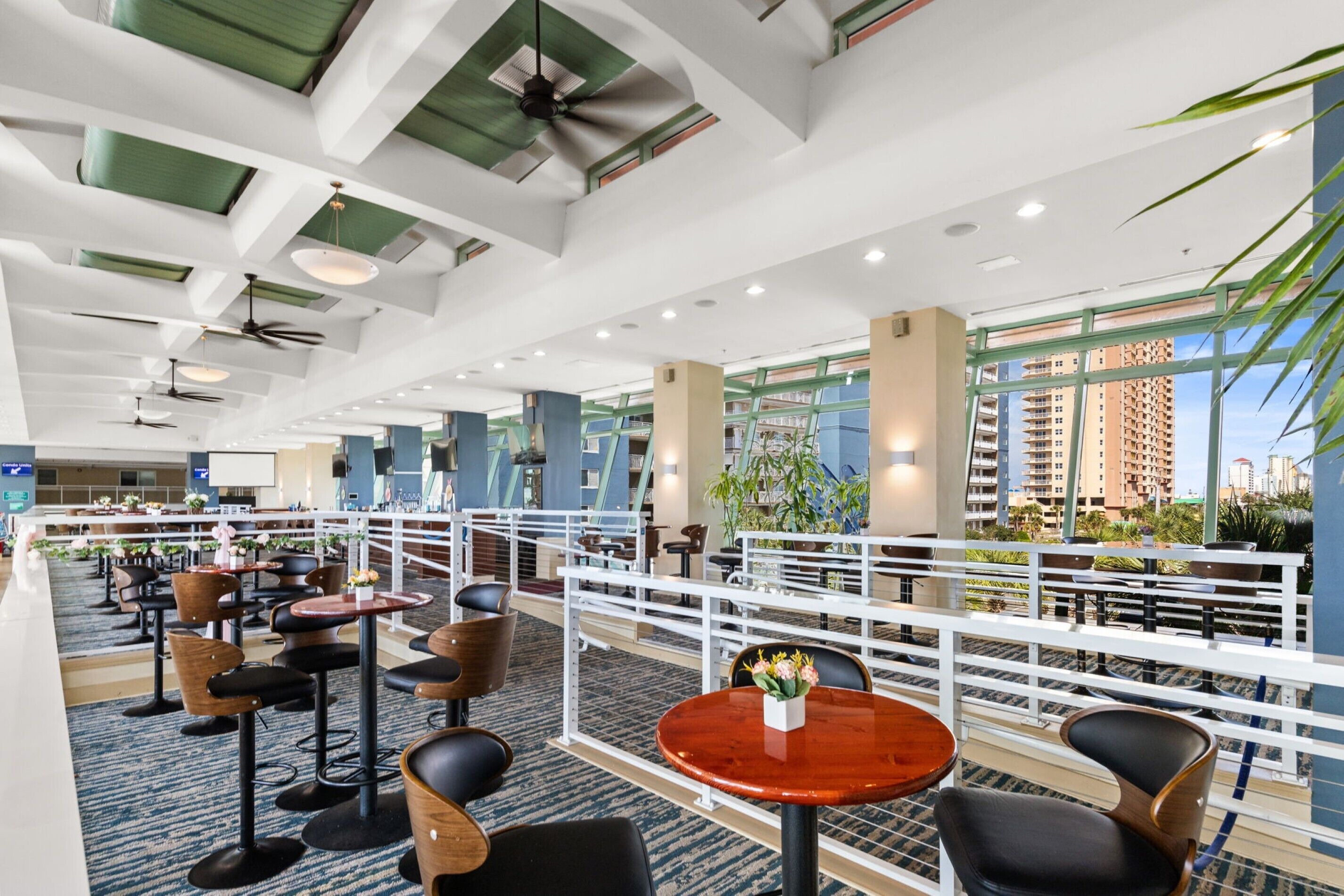 Een hotel lobby met een modern design, met een hoog plafond met ventilatoren, een zithoek met tafels en stoelen, en grote ramen met uitzicht op de stad.