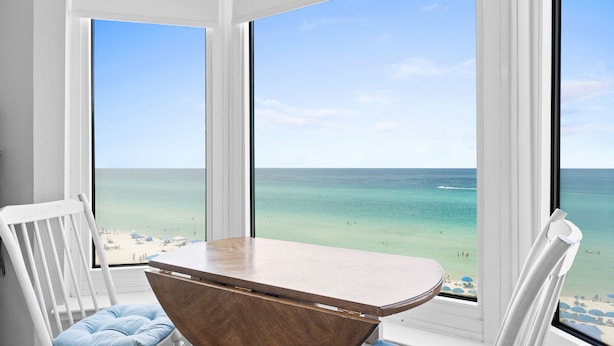 Een kamer met uitzicht op het strand, een houten tafel en witte stoelen.