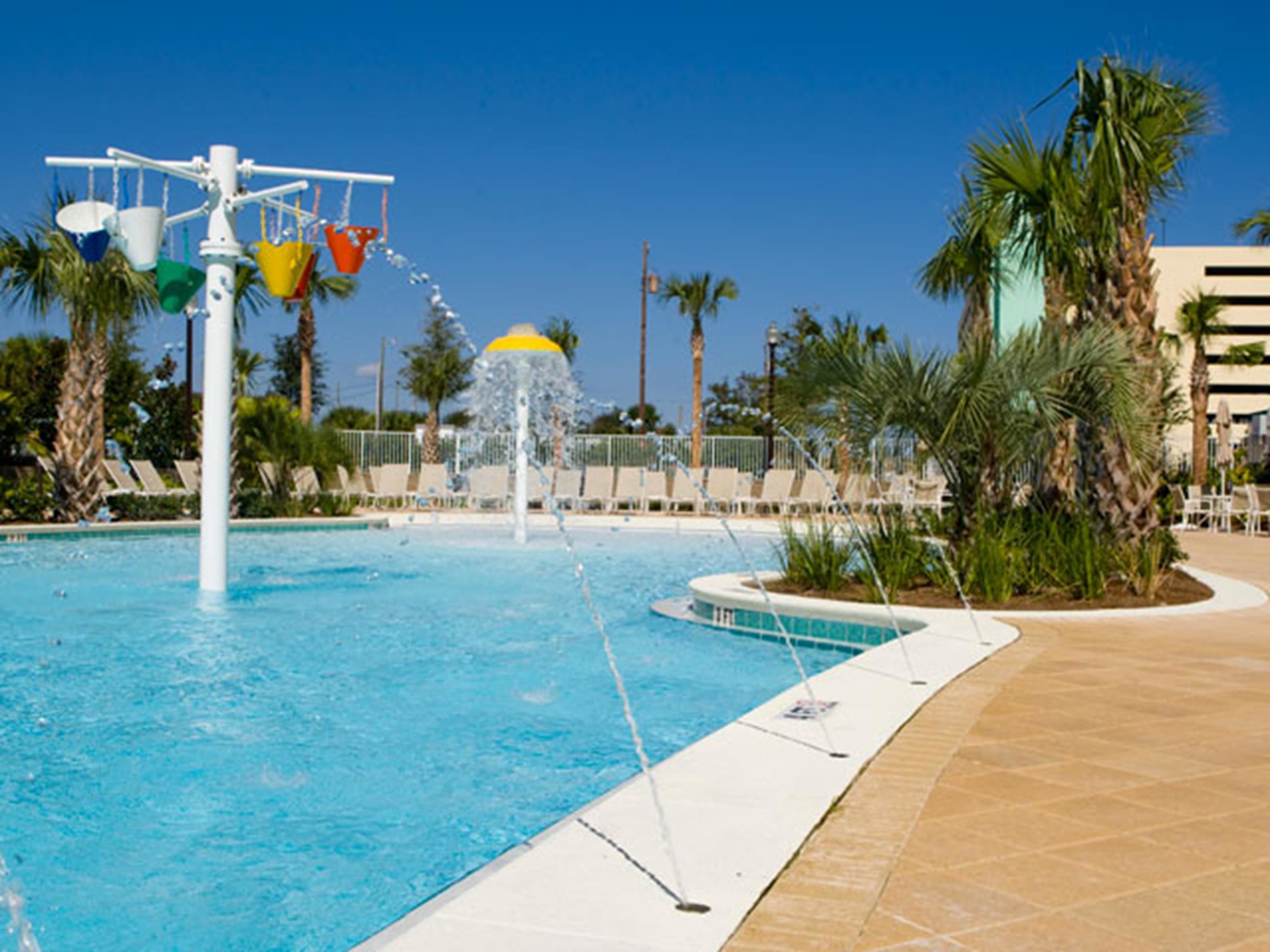 Une piscine agrémentée d’un élément décoratif aquatique, entourée de palmiers et de chaises longues.