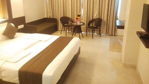Habitación de hotel con una cama grande, un sofá, dos sillones, una mesita con un florero y un televisor.