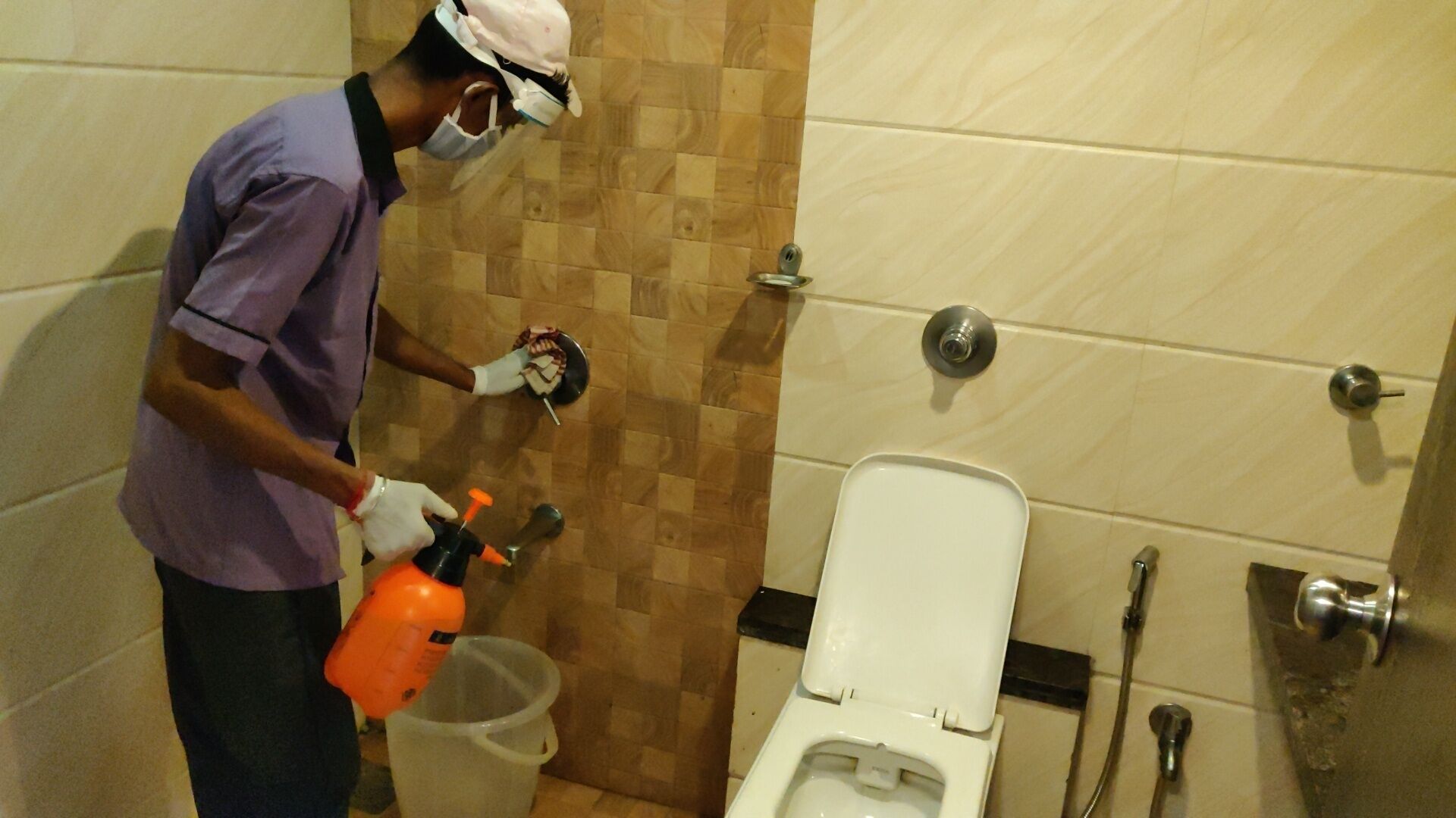 Iemand maakt een toilet schoon met een sprayfles en een emmer.