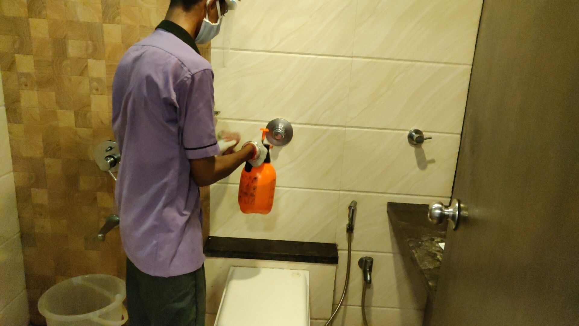 Una persona limpiando un lavamanos de baño con un pulverizador.