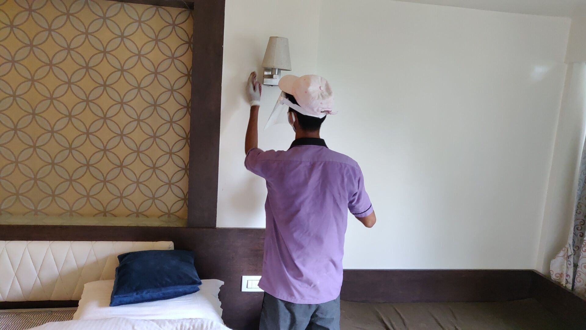 A person in a purple shirt and cap painting a wall.