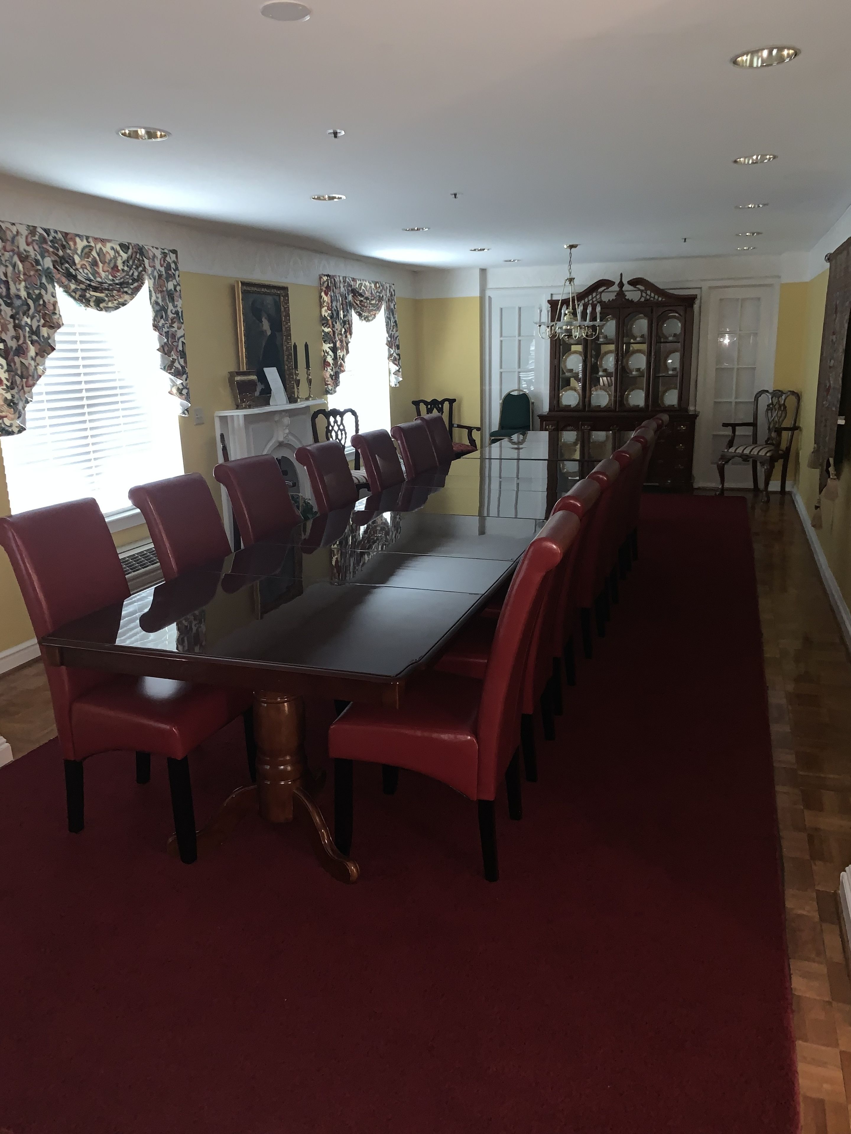 A dining area with a long table and red chairs, a wooden cabinet, and a patterned curtain.